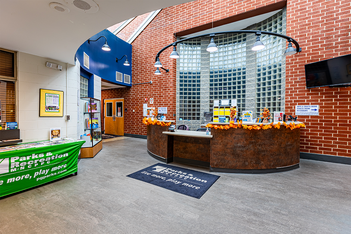 A lobby space with a round reception desk in front of a curved, glass block window in a brick wall. To the left is an information table covered with flyers.