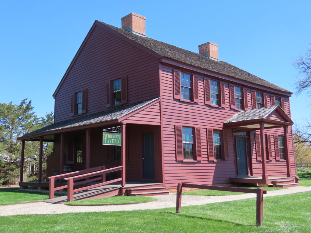 A maroon, two-story clapboard building with a front portico and a side porch.