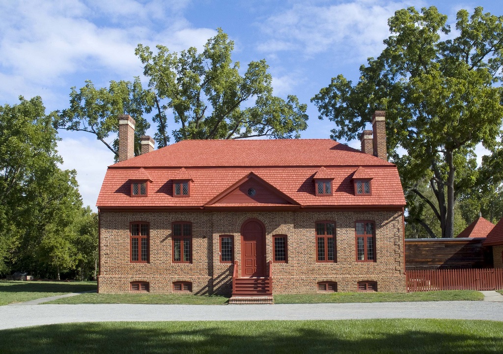 A two-story brick building with a red door, red trim, and a red mansard roof.