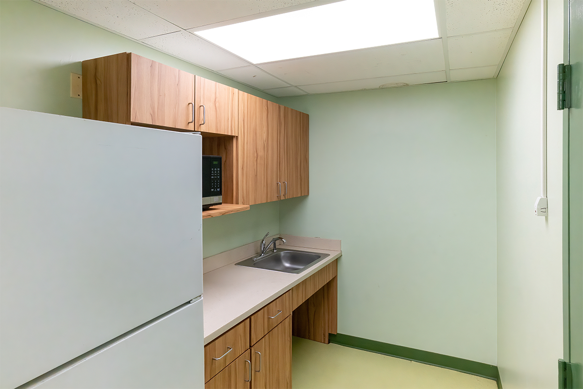Alternate view of a kitchenette with a full-size fridge, microwave, sink, counter, and cabinets.