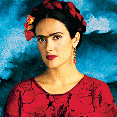 A dark-haired woman wearing a red top and red dangly earrings, with her hair braided into a crown with a red ribbon and roses.