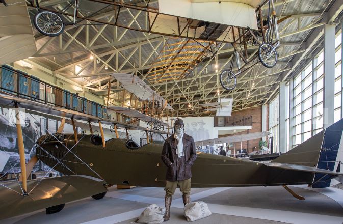 A mannequin dressed as a pilot in front of an old plane in a museum hangar