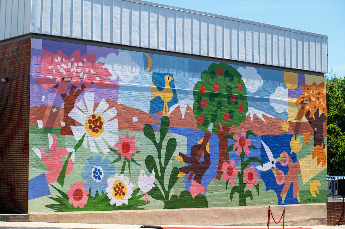 A large, colorful mural covers the side of a large brick building. The mural depicts flowers, trees, and birds in various seasons.