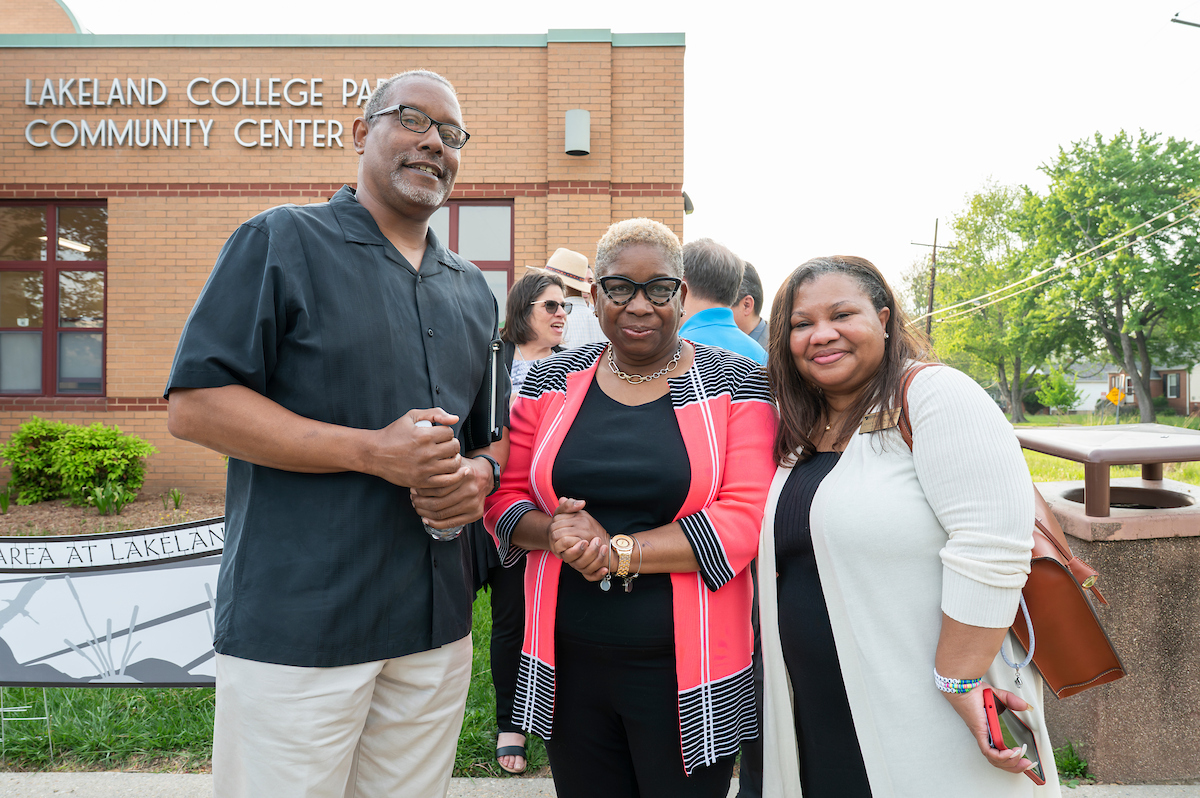 Two women and one man pose smiling outside in front of a brick building with letters on it that read LAKELAND COLLEGE PARK COMMUNITY CENTER.
