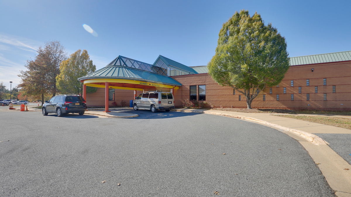 Exterior view of a large brick, glass, and metal building with a blue and yellow portico supported by red columns.