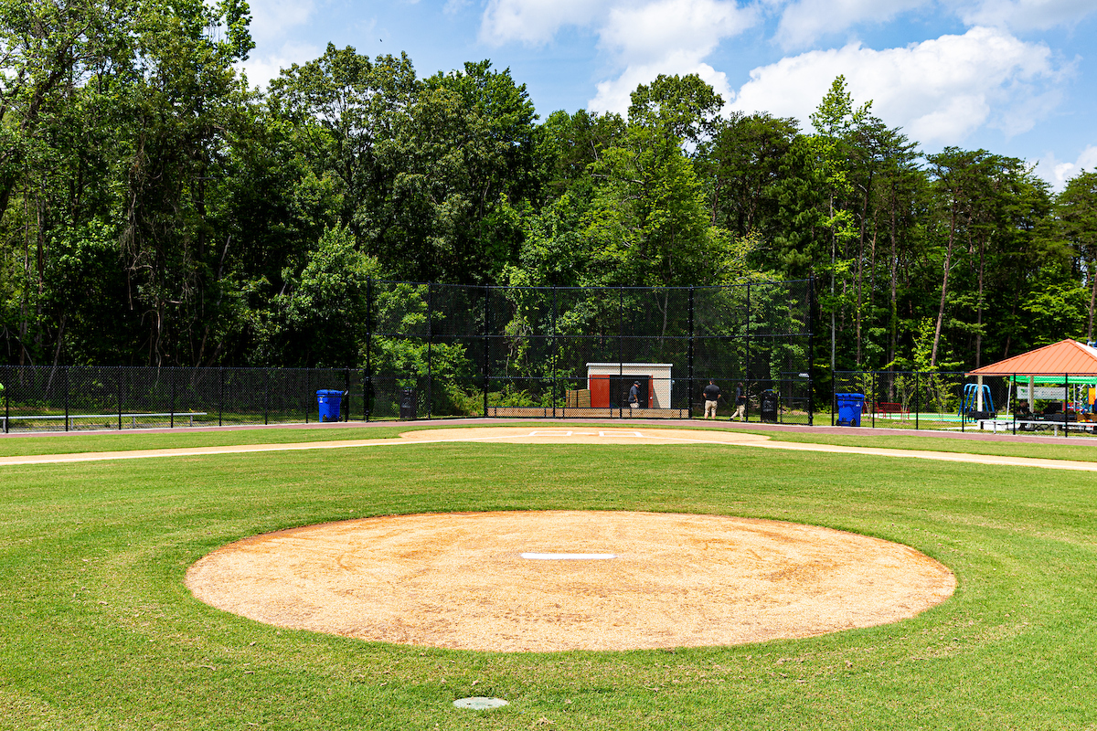 A baseball diamond as seen from behind the pitcher's mound. Behind it, to the right, is a picnic shelter with a playground just visible behind it.