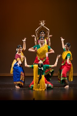 Five female dancers in colorful traditional Indian attire performing a coordinated pose on stage.