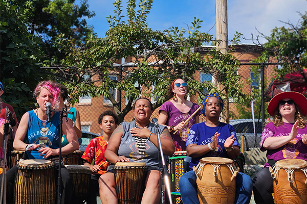 Half a dozen performers singing and playing hand drums in the sunshine.