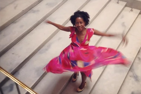 A woman on a wide, marble staircase twirling in a pink patterned dress.
