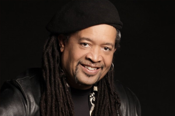Headshot of a smiling man wearing a black leather jacket and a black hat.