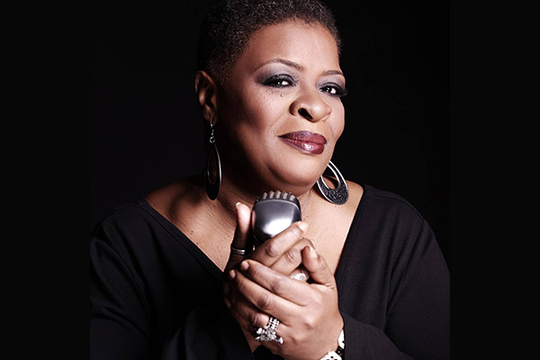 Promotional headshot of a woman wearing silver earrings and cradling a silver microphone in her hands.