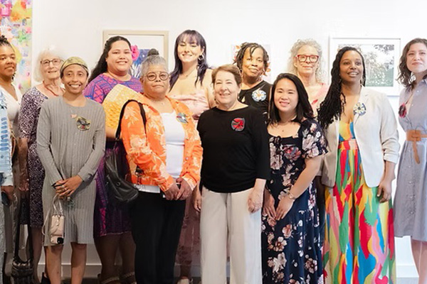 Twelve women pose together in an art gallery.