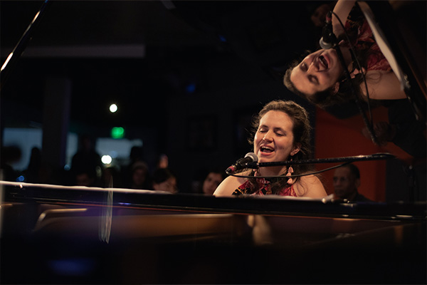 A woman playing a grand piano and singing on a stage.