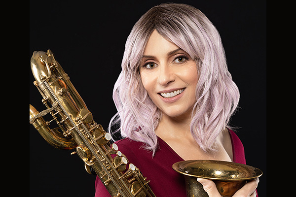 A smiling woman in red poses with a baritone saxophone.