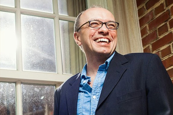 Headshot of a smiling man in a dark jacket and glasses.