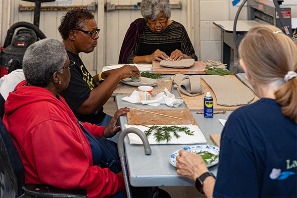 Seniors sit around a table, imprinting leaves and branches onto slabs of clay.