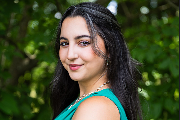 Headshot of a smiling woman in a green top, standing near some trees.