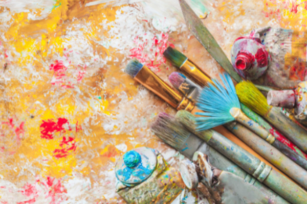 A collection of well-used artist brushes and tubes of paint lying on a painted surface.