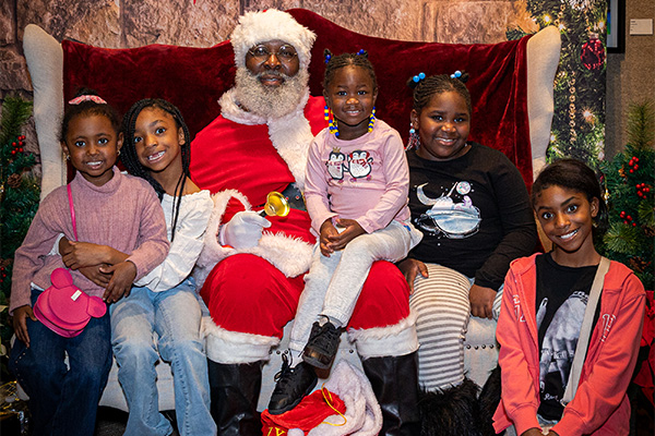 Five smiling kids pose with a man in a Santa suit.