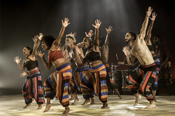 A dance troupe in matching, striped pants performs synchronized choreography on a stage.