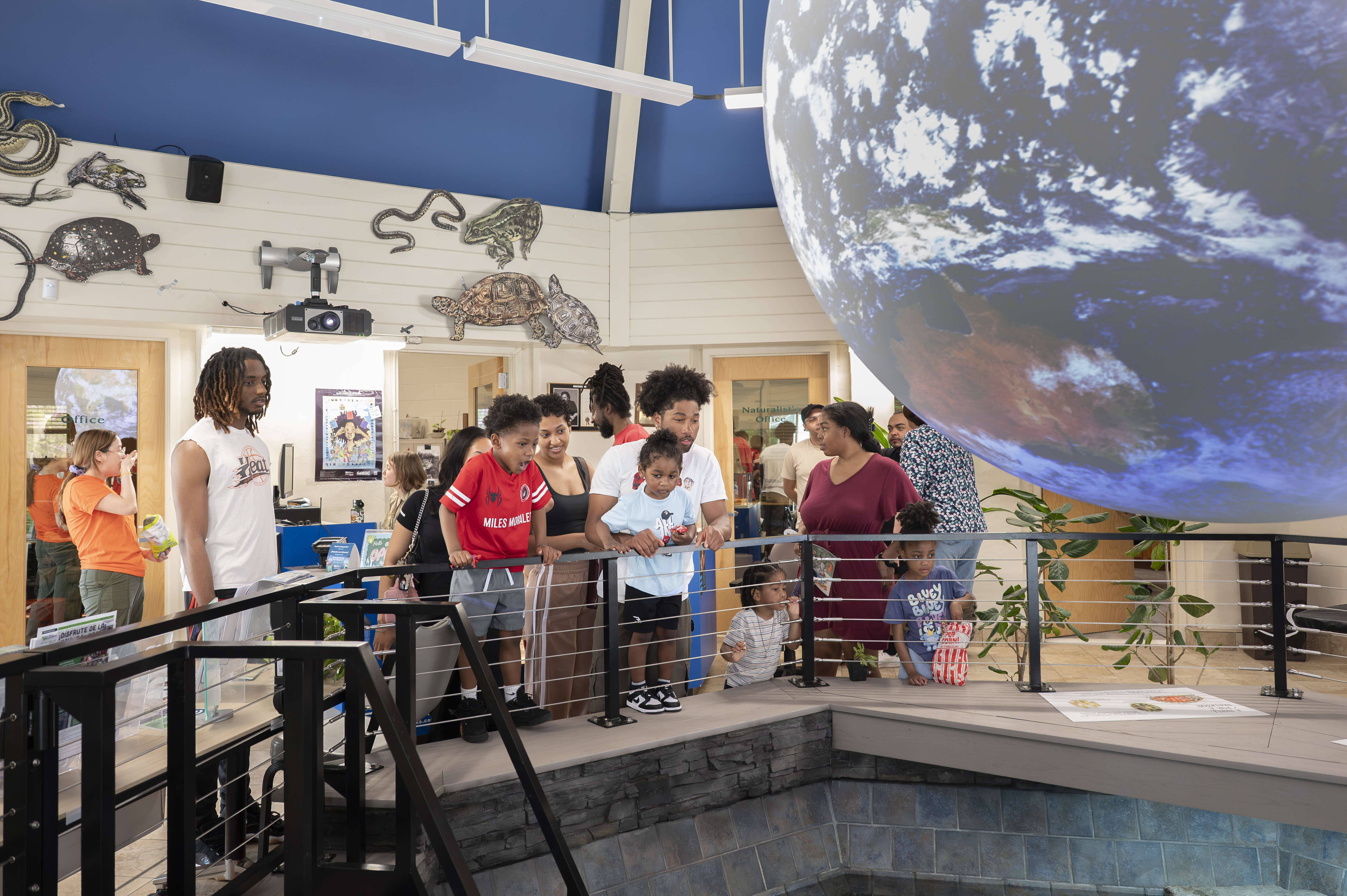 Museum visitors gather around a large suspended globe exhibit, viewing interactive displays and educational exhibits inside a nature center.
